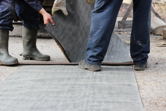 Chantier extérieur avec ouvriers posant des dalles de béton sur une surface préparée