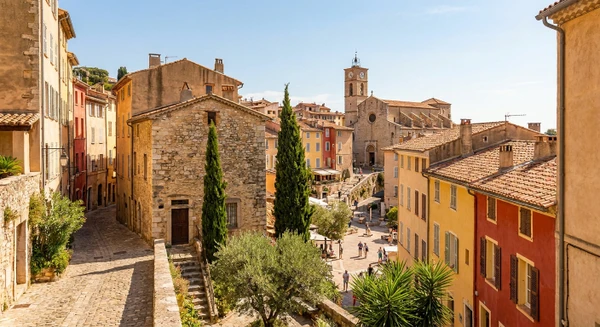 Photographie réaliste de la ville de Grasse, France, montrant des éléments architecturaux et urbains caractéristiques : vue du centre-ville historique avec ses ruelles typiques provençales, ses bâtiments en pierre, ses façades colorées ou terracotta, et ses toits de tuiles. La photo peut inclure des éléments emblématiques comme la cathédrale Notre-Dame-du-Puy, les places publiques du centre-ville, ou une perspective des quartiers reconnaissables de Grasse. La photo doit être prise de jour, bien éclairée, avec une qualité professionnelle, sans texte ni logo visible. Elle doit représenter distinctement Grasse et son caractère provençal pour se démarquer visuellement des images côtières de Cannes, Antibes et Nice.